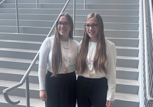 Claire and Emma Uhler stand together with their medals in front of a staircase at the Nebraska State SkillsUSA Leadership and Skills Conference.