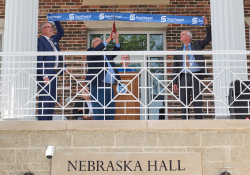 Jon Kisby, Ed Koster and Dr. Paul Illich cut the blue SCC ribbon at Nebraska Hall. All three men are in blue suits. 