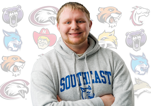 Male student with blonde hair, wearing a Bobcat hoodie is standing in front of Nebraska college mascots. 