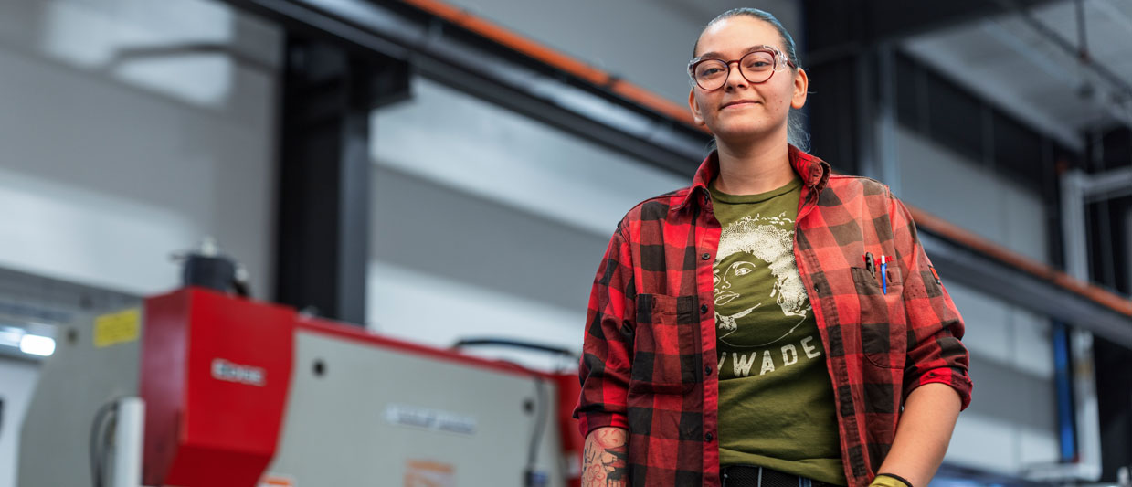 Sapphire Guzman is wearing glasses, a red plaid flannel shirt, and yellow work gloves in SCC’s new Welding Technology Center. 