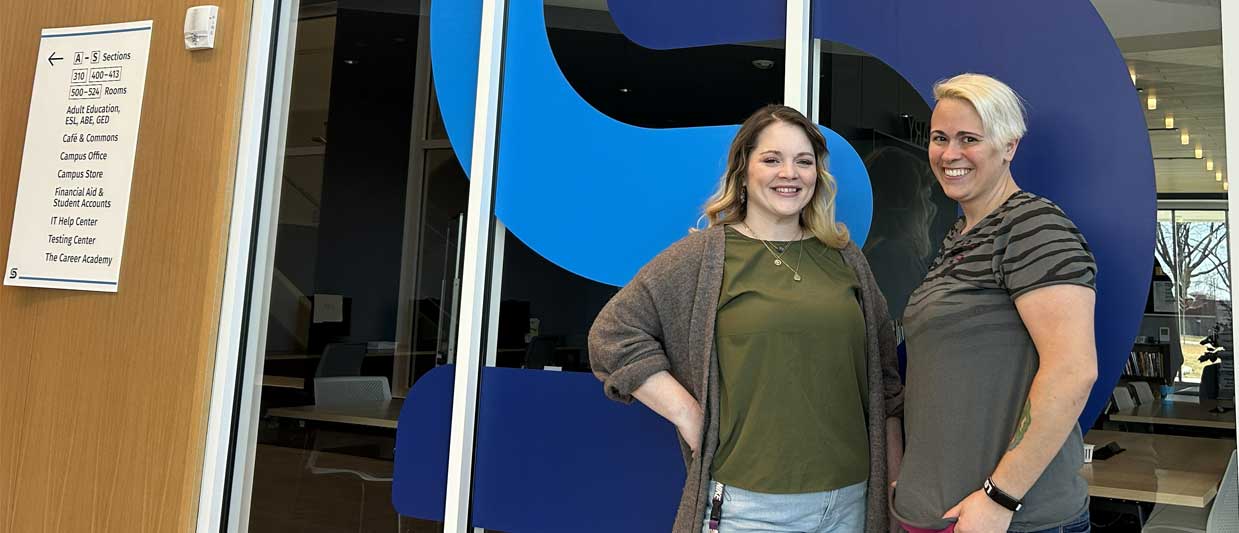 Two women smiling and posing together in front of the Southeast "S" logo on a large window.